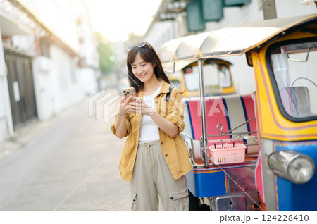 Young Asian woman backpack traveler standing a side of Tuk Tuk taxi on summer vacations at Bangkok, Thailand. Journey trip lifestyle, Asia summer tourism concept. 124228410