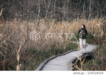 Tranquil trek: A young Asian woman explores a Japanese trail in fall, reveling in the vibrant colors under the silver sky. 124228428