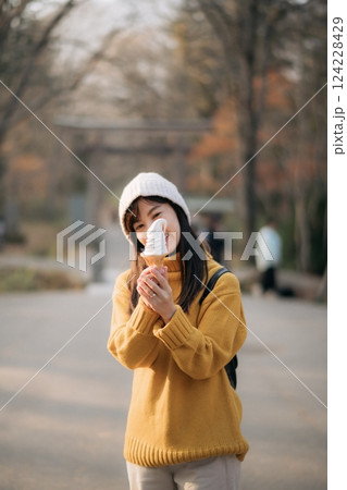 Fashionable Asian woman in yellow sweater holding a pink ice cream cone. Smiling portrait of a cute girl in an ethnic outfit, expressing joy and delight indoors. Fashionable Asian woman in yellow sweater holding a pink ice cream cone. Smiling portrait of a cute girl in an ethnic outfit, expressing joy and delight indoors. 124228429