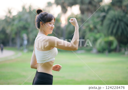 Strong fitness asian woman runner showing off muscular arms flexing biceps. wellbeing success concept. Strong fitness asian woman runner showing off muscular arms flexing biceps. wellbeing success concept. 124228476