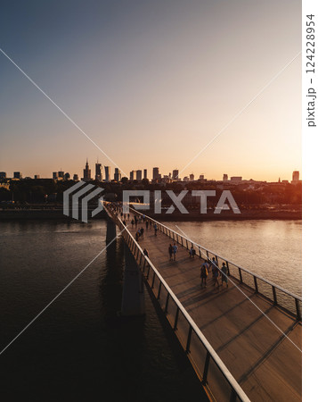 newly built pedestrian and bicycle modern bridge over Vistula river at sunset, downtown financial district and contemporary architecture of Warsaw city skyline, aerial top view 124228954