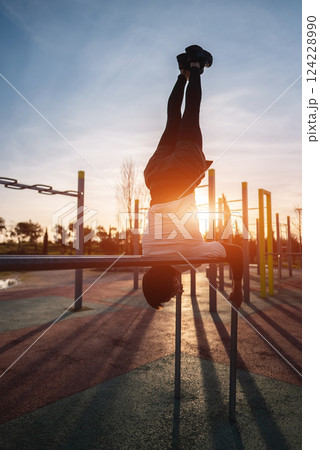 young athletic man exercising at fitness calisthenics workout and do handstand in parallel bars at street gym during sunset, body improvement and strength training concept 124228990