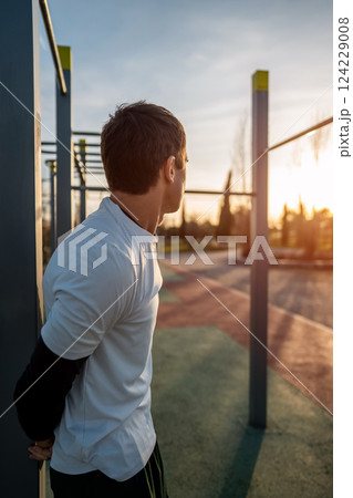 young athletic man resting after fitness calisthenics workout at street gym during sunset, taking a break during body improvement and strength training 124229008
