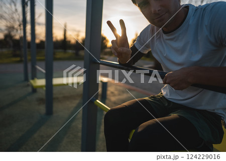 cheerful athletic man resting after exercising abs bench crunch at fitness calisthenics workout at street gym during sunset, relax after body improvement and strength training concept 124229016