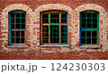 An old red brick wall with three wooden windows painted green, blue and yellow 124230303