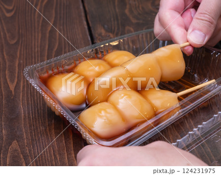 プラスチック容器に入っている和菓子。甘い醤油タレの"みたらし団子"を持った人の手。 プラスチック容器に入っている和菓子。甘い醤油タレの"みたらし団子"を持った人の手。 124231975