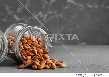Shelled almonds spilling from glass jar onto gray surface, creating visually appealing arrangement with potential use in healthy food and lifestyle contexts Shelled almonds spilling from glass jar onto gray surface, creating visually appealing arrangement with potential use in healthy food and lifestyle contexts 124232495