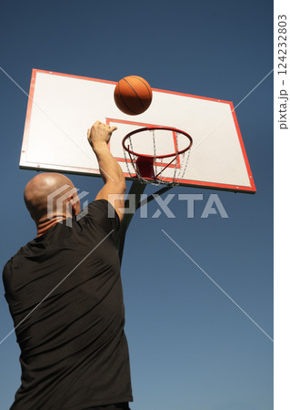 Basketball player or sporty man tries to throw ball into basketball hoop on sports court at courtyard. Street style. Game moment. Close up. Basketball player or sporty man tries to throw ball into basketball hoop on sports court at courtyard. Street style. Game moment. Close up. 124232803