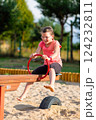Happy young girl playing on a wooden seesaw at a playground, holding red handles and smiling while enjoying outdoor fun on a sunny day 124232811