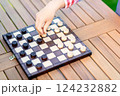 Close-up of a hand moving a piece on a wooden checkers board during an outdoor game, focusing on strategy and decision-making 124232882