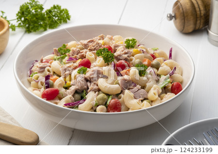 Homemade macaroni salad with elbow pasta and canned tuna, carrot, Purple cabbage, corn, tomato, green peas and mayonnaise dressing in a white plate on wooden table. 124233199