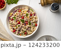 Homemade macaroni salad with elbow pasta and canned tuna, carrot, Purple cabbage, tomato, corn, green peas and mayonnaise dressing in a white plate on wooden table.Top view 124233200