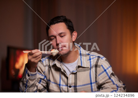 Young man eating sushi from home delivery pointing and showing with thumb up to the side with happy face smiling 124234896