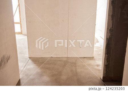The room is under construction with a rough finish, plastered walls, concrete floor. Wiring of ventilation pipes on a concrete ceiling in a house under construction. 124235203
