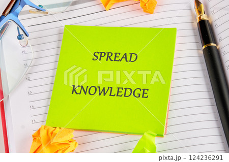 A bright sticky note emphasizes the important message to spread knowledge amidst writing materials and stationery in a study environment 124236291