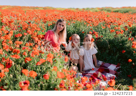 Happy family: mother with daughters in a blooming poppy field. Beauty smiling woman and kids in dress with red flowers Happy family: mother with daughters in a blooming poppy field. Beauty smiling woman and kids in dress with red flowers 124237215