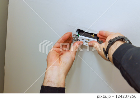 Electrician person is carefully placing an electrical outlet into ceiling of home installation 124237256