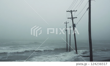 Misty coastal scene with broken wooden poles and a damaged power line standing in rough ocean waves. Misty coastal scene with broken wooden poles and a damaged power line standing in rough ocean waves. 124238317