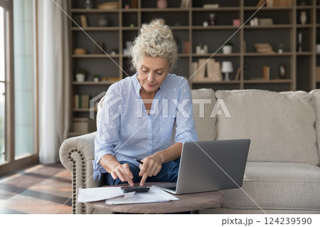Woman pensioner engaged in finance paperwork at cozy home office 124239590
