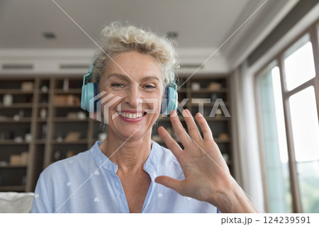 Mature woman in headphones looking at web camera waving hand Mature woman in headphones looking at web camera waving hand 124239591