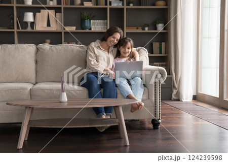 Single mother embrace little daughter using notebook at living room 124239598