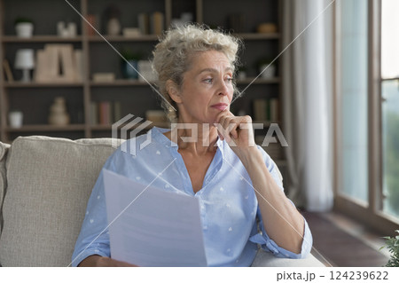 Doubtful senior woman retiree sit on sofa hold business documents Doubtful senior woman retiree sit on sofa hold business documents 124239622