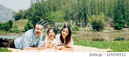Asian family father mother and daughter lying on blanket spring meadow field grass in park cheerful sweet kid girl, parents and child picnic enjoying outdoors together, Family relaxation concept 124240512
