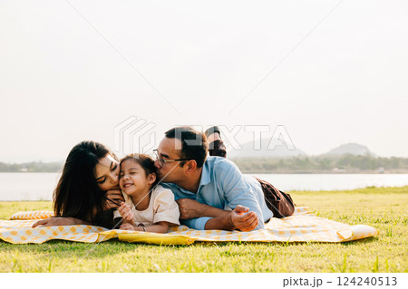 Asian family father mother and daughter lying on blanket spring meadow field grass in park cheerful sweet kid girl, parents and child picnic enjoying outdoors sunset time together, Family relaxation 124240513