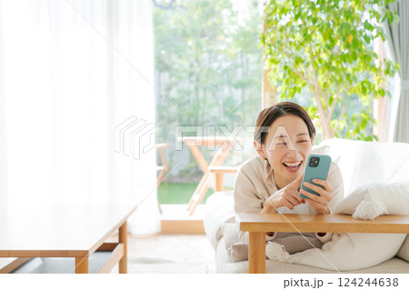 ソファに寝転んでスマホを見る女性 124244638