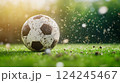 Soccer ball on a grassy field, partially covered in dirt, with grass and soil particles flying around	 124245467
