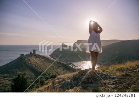 A blonde woman stands on a hill overlooking the ocean. She is wearing a white dress and she is enjoying the view. A blonde woman stands on a hill overlooking the ocean. She is wearing a white dress and she is enjoying the view. 124248291
