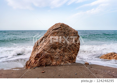Beach boulder seascape: Wave laps rock on sandy beach, sunny day for tranquil scene. 124248295