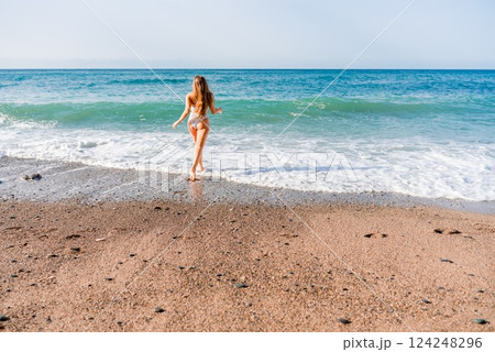 Happy woman in bikini running on the beach. Active leisure, a beautiful girl in a bikini is having fun on the beach, big waves are splashing along the beach. 124248296