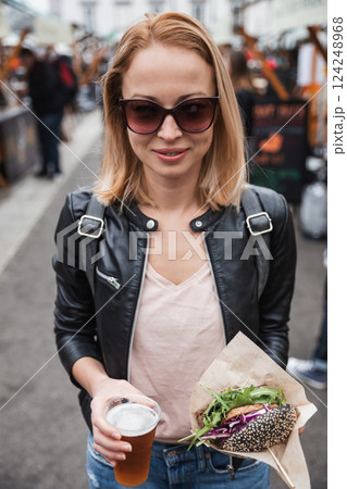 Beautiful young woman holding delicious organic salmon vegetarian burger and homebrewed IPA beer on open air beer an burger urban street food festival in Ljubljana, Slovenia 124248968