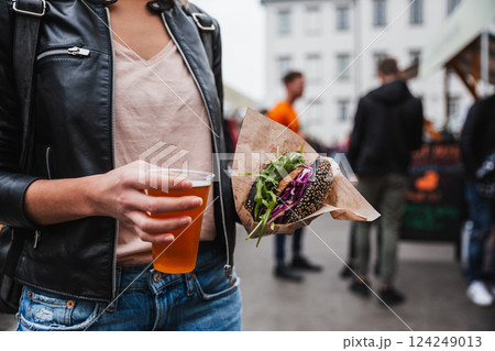 Close up of woman hands holding delicious organic salmon vegetarian burger and homebrewed IPA beer on open air beer an burger urban street food festival in Ljubljana, Slovenia 124249013