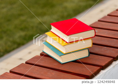 Three colorful books stacked horizontally on park wooden bench. 124249848