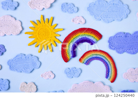 Knitted toys blue and white clouds, yellow sun, rainbow on blue background. Baby stuff and accessories. Top view, flat lay, banner Knitted toys blue and white clouds, yellow sun, rainbow on blue background. Baby stuff and accessories. Top view, flat lay, banner 124250440