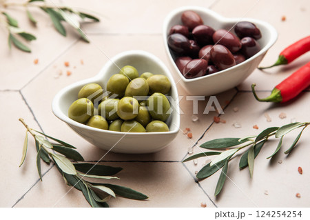 Heart shaped bowls containing green and black olives, olive branches, chili peppers and himalayan salt on tiled surface Heart shaped bowls containing green and black olives, olive branches, chili peppers and himalayan salt on tiled surface 124254254