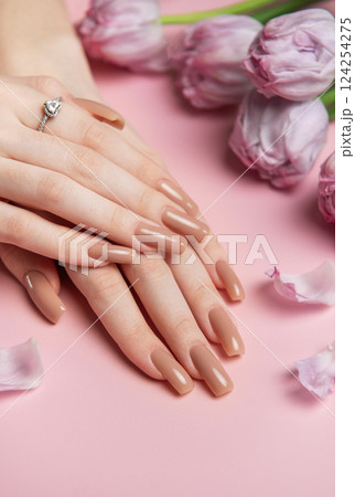 Woman showing stylish nude manicure near pink tulips on pink background Woman showing stylish nude manicure near pink tulips on pink background 124254275