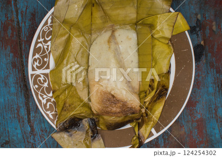 Traditional Tamal Pisque stuffed in banana leaf served on wooden table, Central American typical food Tamal Pisque stuffed. Stuffed tamale served on wooden table 124254302