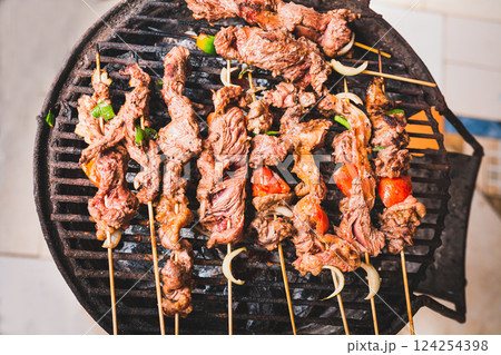 Homemade roast meat skewers on charcoal grill. Charcoal roasted meat skewers. Top view of meat roasted on a grill Homemade roast meat skewers on charcoal grill. Charcoal roasted meat skewers. Top view of meat roasted on a grill 124254398
