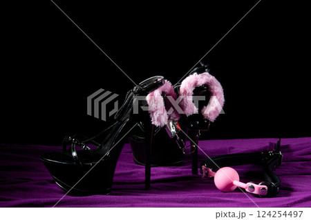 Adult sex games. Kinky lifestyle. Pink gag ball, handcuffs and a pair of black high-heeled shoes on the purple bedsheet. Bdsm outfit 124254497
