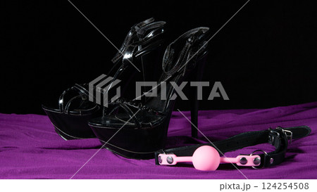 Adult sex games. Kinky lifestyle. Pink gag ball and a pair of black high-heeled shoes on the purple bedsheet. Bdsm outfit 124254508