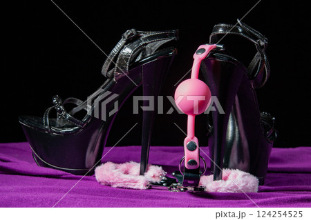 Adult sex games. Kinky lifestyle. Pink gag ball, handcuffs and a pair of black high-heeled shoes on the purple bedsheet. Bdsm outfit 124254525