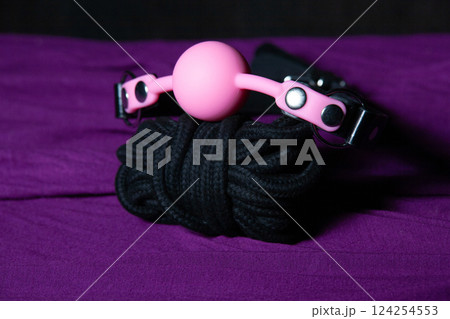 Bdsm outfit. Bondage and Gag ball on the purple bedsheet. Adult sex games. Kinky lifestyle. Bdsm outfit. Bondage and Gag ball on the purple bedsheet. Adult sex games. Kinky lifestyle. 124254553