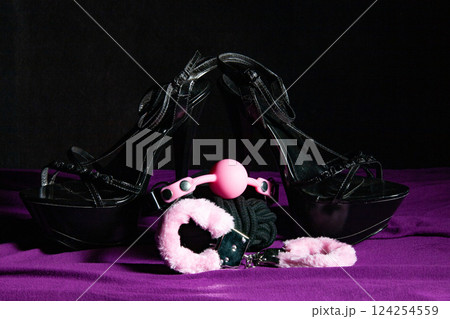 Adult sex games. Kinky lifestyle. Pink gag ball, handcuffs and a pair of black high-heeled shoes on the purple bedsheet. Bdsm outfit 124254559