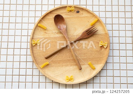 time to eat pasta. wooden plate with fork and spoon in form of clock hands. pasta on plate. time to eat pasta. wooden plate with fork and spoon in form of clock hands. pasta on plate. 124257205