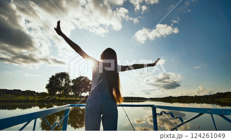 Young woman with open arms enjoying the sunset by the lake, feeling a sense of freedom and happiness Young woman with open arms enjoying the sunset by the lake, feeling a sense of freedom and happiness 124261049