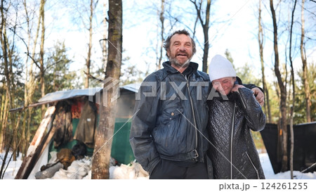 Homeless couple hugging near ramshackle shelter, winter forest revealing hardship of addiction and economic struggle Homeless couple hugging near ramshackle shelter, winter forest revealing hardship of addiction and economic struggle 124261255