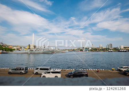 Russian naval vessels moored at vladivostok harbor, golden suspension bridge spanning scenic maritime backdrop under bright sunlight 124261268